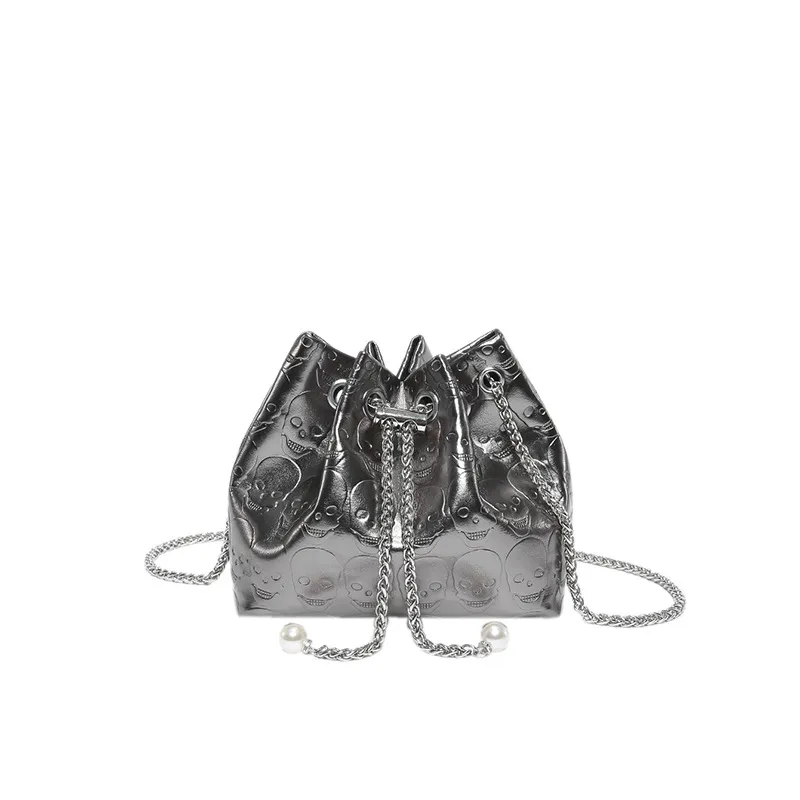 A stylish metallic silver drawstring bag with an embossed skull pattern. The bag features a chain drawstring closure with pearl accents at the ends, along with a matching silver chain shoulder strap. Its edgy yet elegant design makes it a fashionable accessory for various occasions.