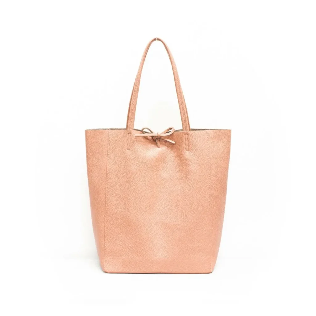 A minimalist tote bag in soft pink pebbled leather featuring a lace-up closure with a delicate bow at the top. The bag has a spacious, unstructured design with two slim shoulder straps, making it a stylish and functional accessory for everyday use. Its elegant and simple aesthetic enhances versatility for various occasions.